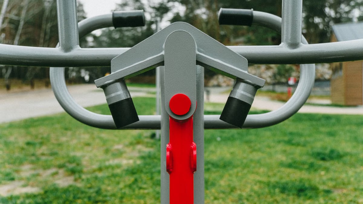 Outdoor exercise equipment with focus on red detail, set in a lush Polish park during spring.